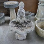 A concrete figural cherub on a shell garden bird bath