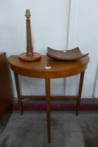 A teak demi-lune hall table, a table lamp and a fruit bowl