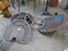 Two vintage cast iron tractor seats, a steering wheel and two cast iron wheels