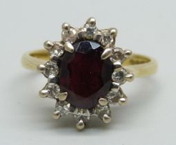 An 18ct gold ring set with a garnet and diamond halo, 4.3g, K