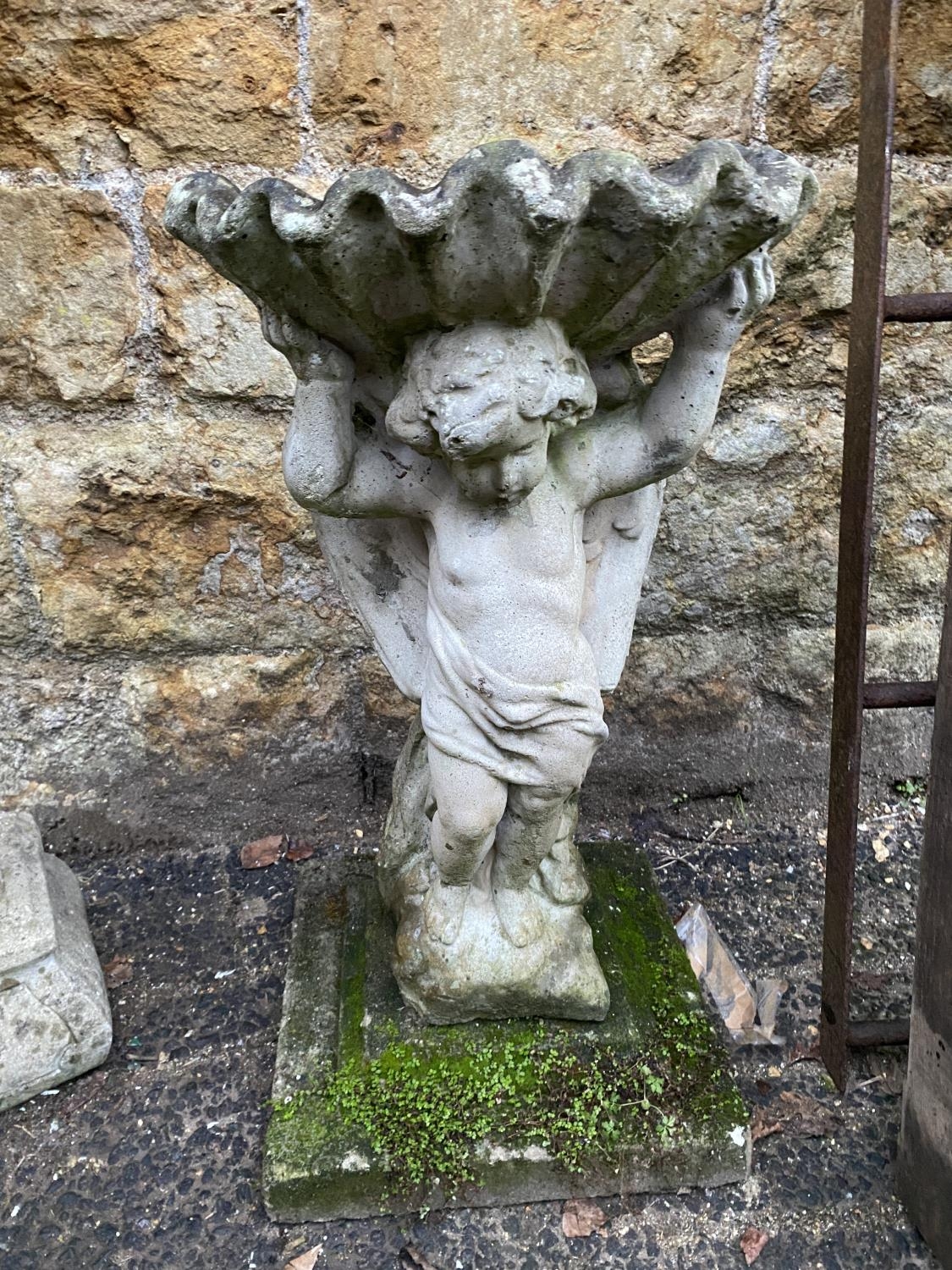 A composite stone bird bath of a cherub supporting a shell, 68cmH