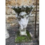 A composite stone bird bath of a cherub supporting a shell, 68cmH