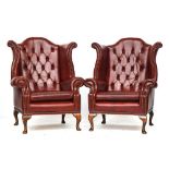 A pair of oxblood leather button upholstered wingback armchairs of recent manufacture, on cabriole