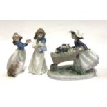 A Lladro figurine, no. 5460, girl with two puppies in a wheelbarrow, together with two Nao
