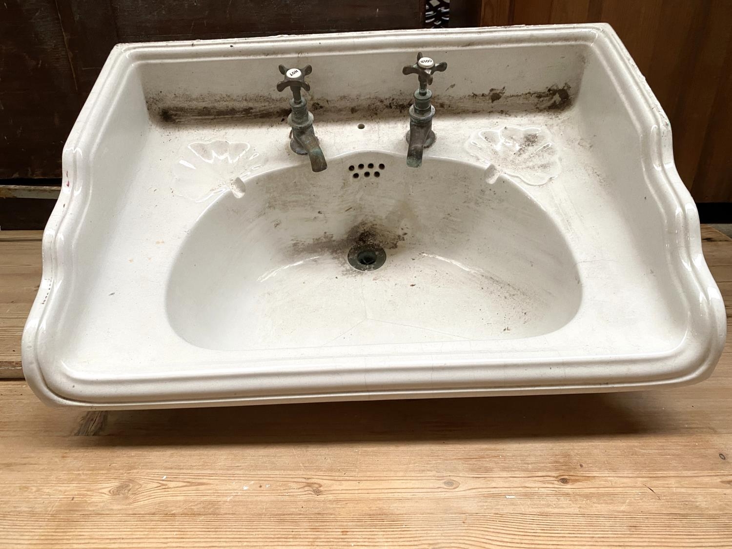 An early 20th century wash basin, with brass taps and plughole, with cast metal wall mount (af),