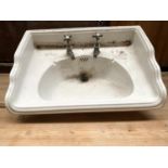 An early 20th century wash basin, with brass taps and plughole, with cast metal wall mount (af),