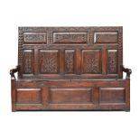 A 17th century carved tavern settle, carved panelled back, downward sloping arms, hinged seats,