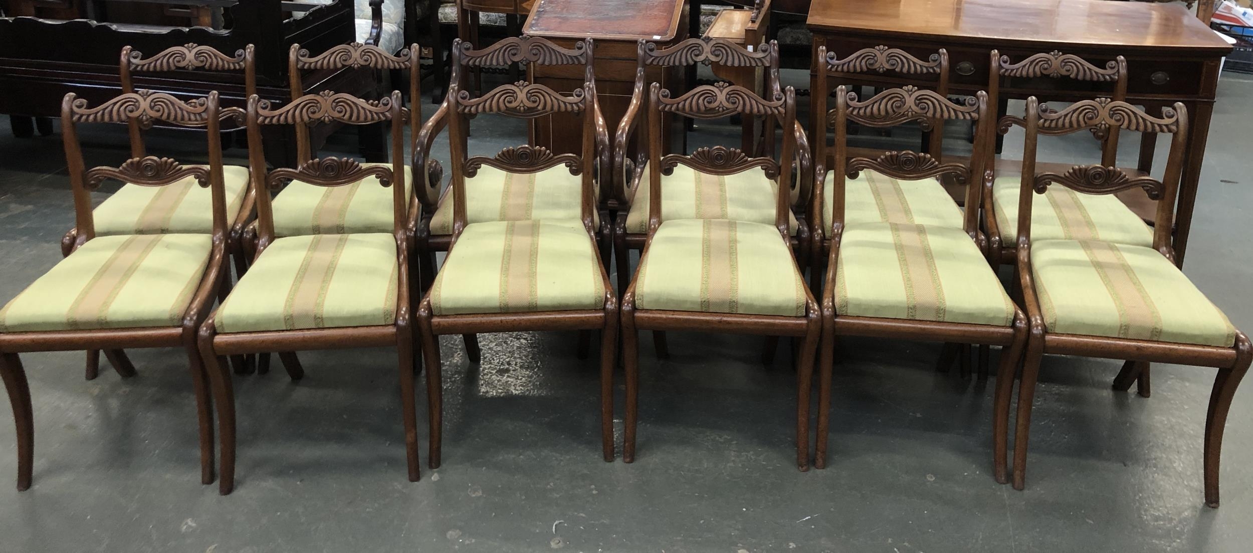 A set of twelve Regency style mahogany dining chairs, carved rails, drop in upholstered seats over