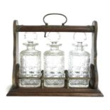 An oak three decanter tantalus with originally plated mounts, with three square cut glass decanters,