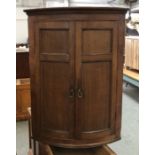 A George III oak bowfront corner cupboard, panel doors opening to a painted interior with three