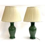 A pair of green glazed baluster form table lamps with cream coloured shades, 69cmH to top of shade