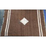A brown camel hair rug with central serrated lozenge and white stripes, 191x131cm