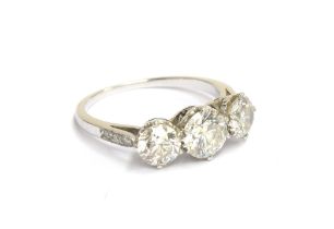 An 18ct white gold diamond trilogy ring, the shoulders studded with diamonds, the three brilliant cu