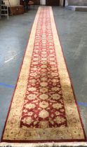 A very long red ground wool runner rug, approx. 12m long, 1m wide