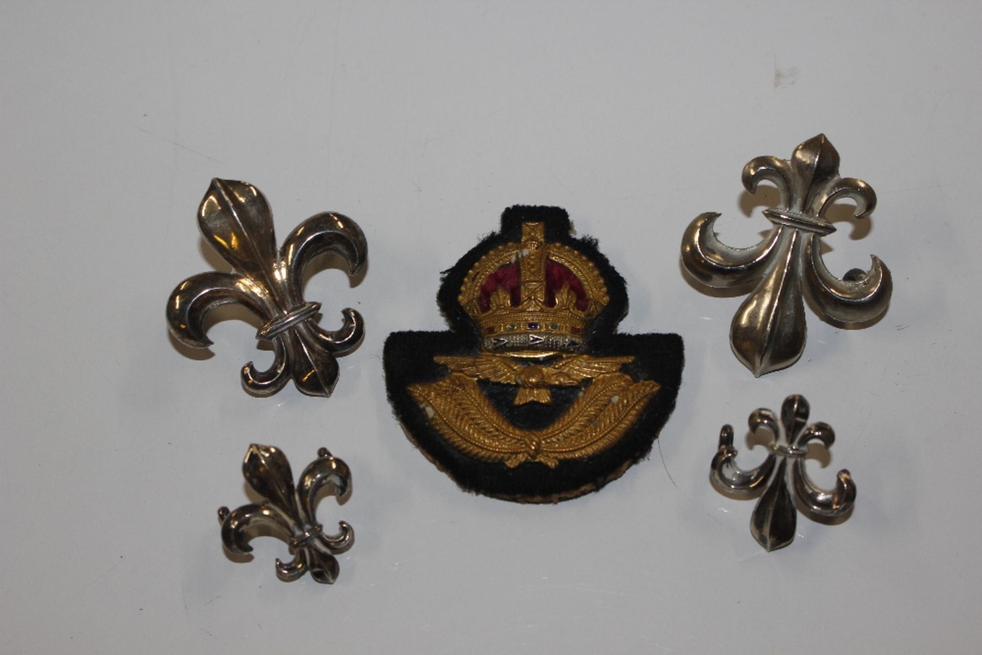 One silver and three white metal Fleur de Lys; and an RAF badge - vendor states to Mervyn Knowles