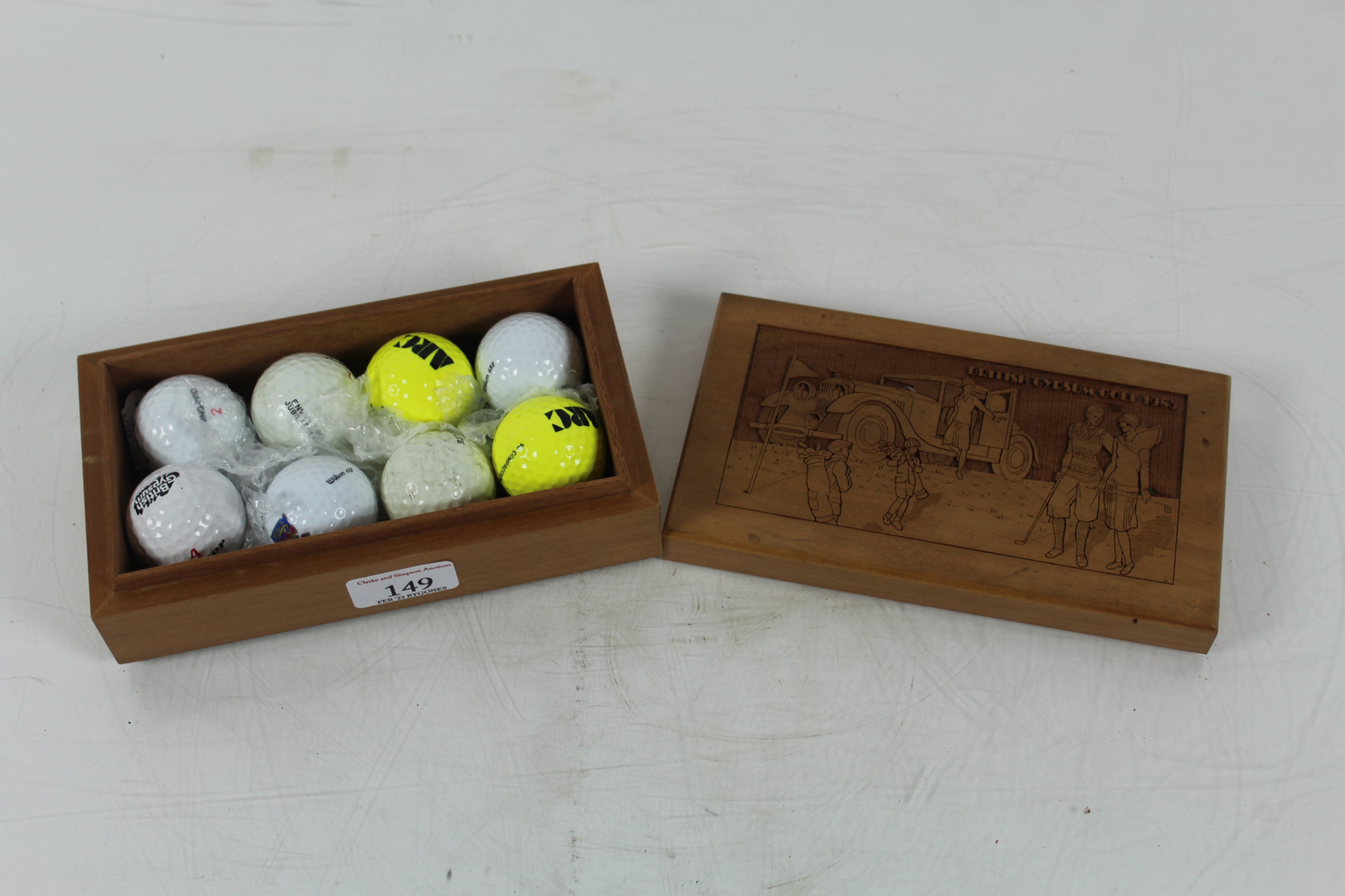 A vintage wooden presentation box containing eight unused golf balls, the lid well carved with