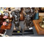 A pair of bronze cherub figures mounted on plinths