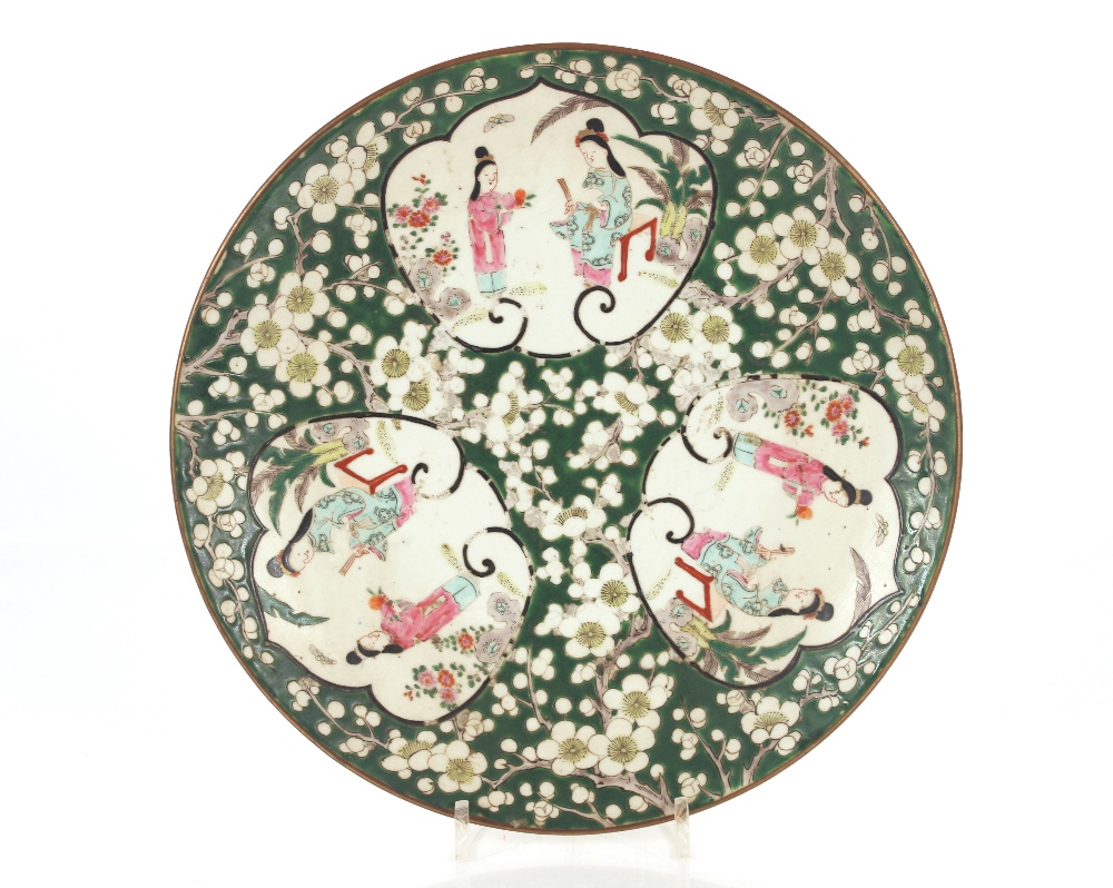 A Chinese plate decorated with three vignettes depicting ladies in garden settings, on a green and