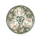 A Chinese plate decorated with three vignettes depicting ladies in garden settings, on a green and