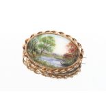 A fine quality oval porcelain brooch, painted with a landscape scene in yellow metal surround