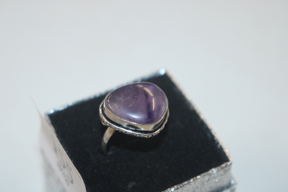 A white metal ring set with amethyst coloured ston