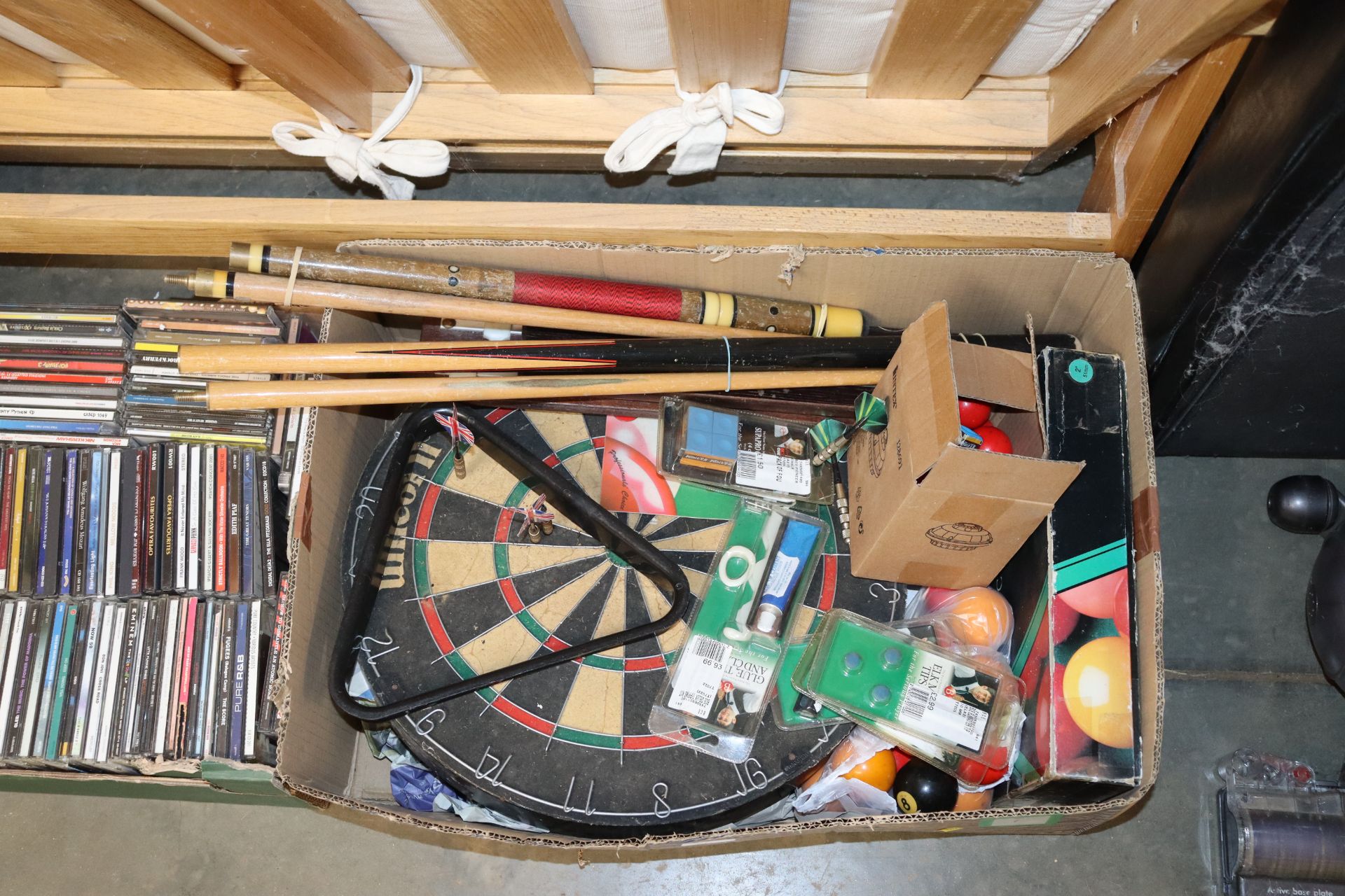 A box containing pool cues, dart boards, darts, sn