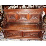 A 19th Century carved oak hall settle, decorated with panels of figures within trailing foliate