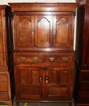 An antique oak livery cupboard, the upper section surmounted by a stepped canopy above cupboards,