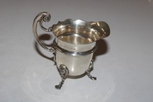 A silver cream jug raised on three paw supports wi