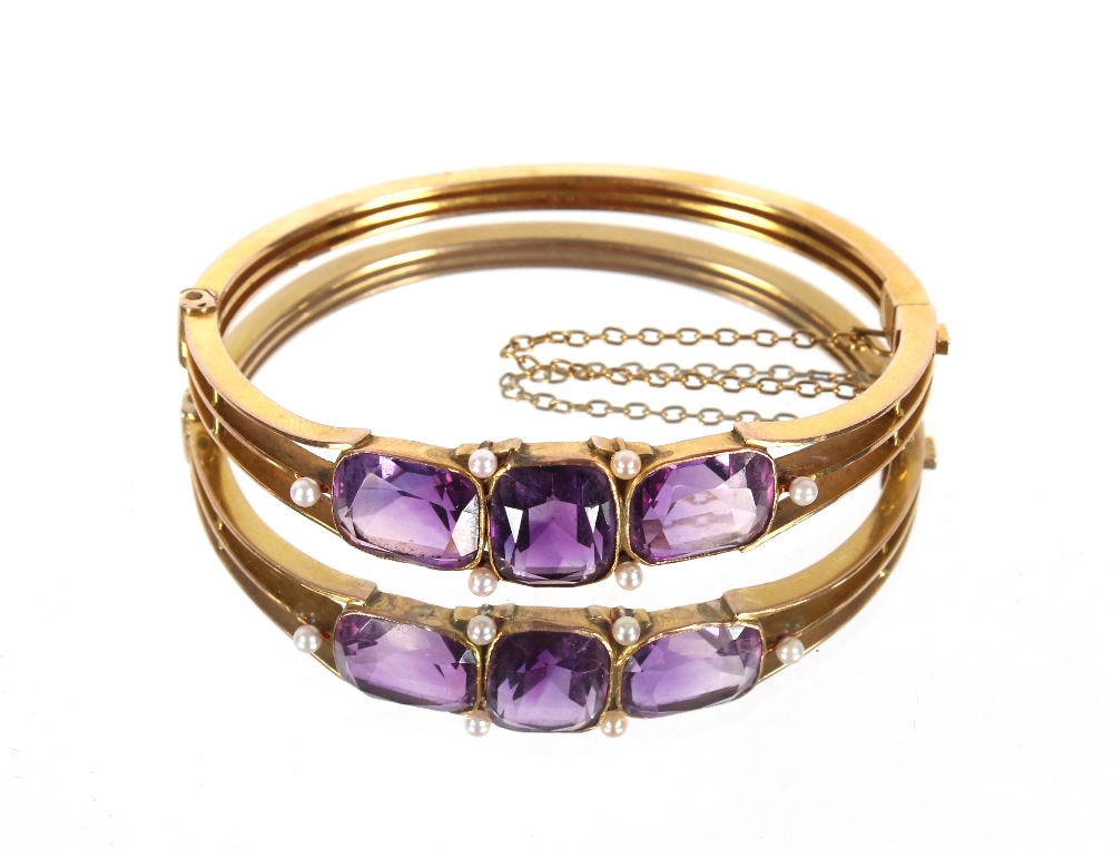 A Victorian unmarked gold bangle set three amethyst stones, flanked by seed pearls with safety chain