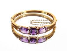 A Victorian unmarked gold bangle set three amethyst stones, flanked by seed pearls with safety chain
