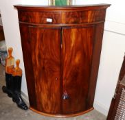 A 19th Century mahogany elliptical hanging corner cupboard, the interior shelves and drawer enclosed