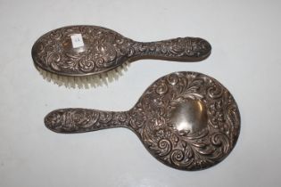 A silver hand mirror and brush with embossed flora