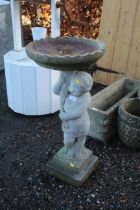 A concrete bird bath in the form of a cherub