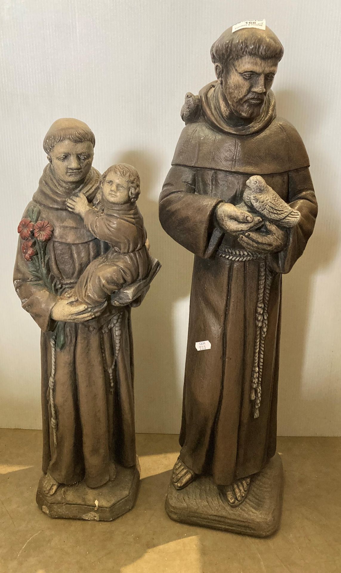 Two concrete statues of monks, one holding a dove, 75cm high and one holding a young child,