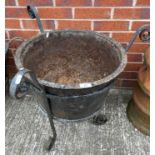 A cast metal cauldron planter in a metal basket,