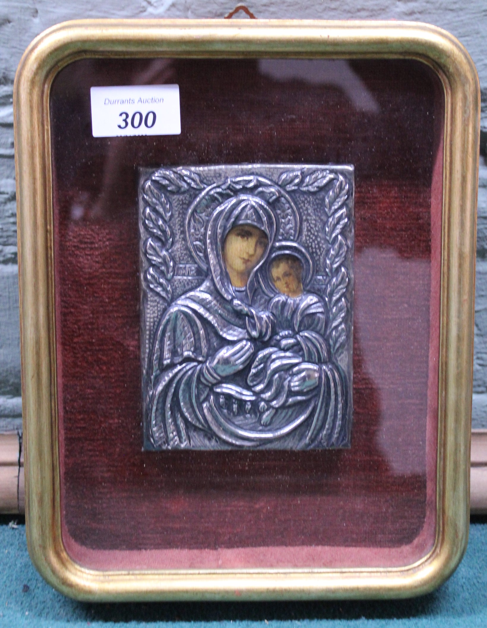 A small white metal covered religious icon housed in a glazed frame depicting the Madonna and Child,