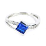 A 9ct white gold dress ring, with central dark blue square cut stone in tension setting, with tiny d