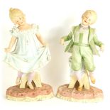 A pair of late 19thC bisque porcelain figures of a girl and boy, in standing pose, on a naturalistic