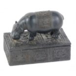 A black painted plaster trinket box, the lid surmounted with a hippopotamus, carved to the side with