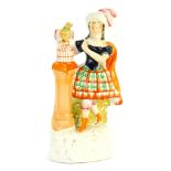 A Staffordshire flat back figure of a Scottish lady, with plinth and bird atop a cage, 24cm high.