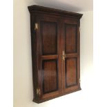 A George III oak hanging corner cupboard, with dentil moulded cornice, two doors with mahogany cross
