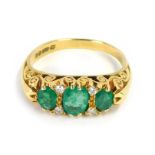 An 18ct gold emerald and diamond gypsy ring, set with three oval cut emeralds and four tiny diamonds