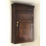 A George III oak hanging corner cupboard, with moulded top, and mahogany cross banding, oval shelf t