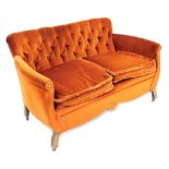 An early 20thC sofa, with button back, shaped arms with brass studs and loose cushions, on castors,