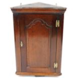 A late 18th oak hanging corner cabinet, with a moulded cornice above a panelled door, with engraved