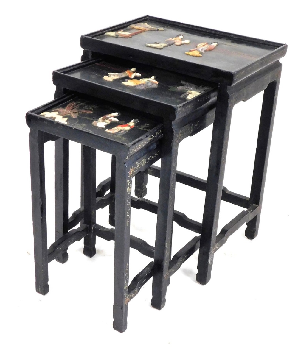 A Chinese black lacquered and hardstone inlaid nest of occasional tables, each glazed top decorated