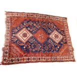 A Qashqai red ground rug, with three central medallions flanked by flowers against a blue ground, wi