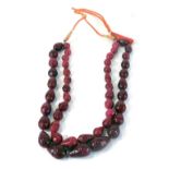 A reconstituted ruby two strand beaded necklace, with pear shaped carved beads, on a black string st