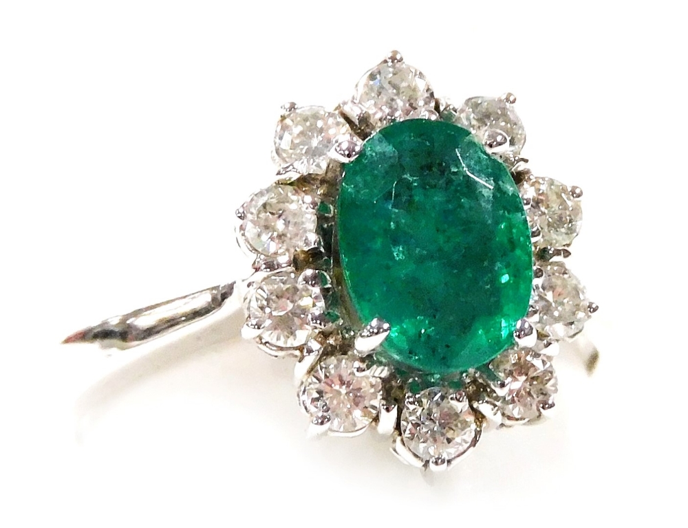 An 18ct white gold emerald and diamond ring, the oval cut emerald in a surround of brilliant cut dia